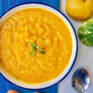 carrot and sage soup in a white and blue bowl on a blue cloth.