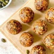 oatmeal bliss balls on a wooden board next to a bowl of pumpkin seeds.