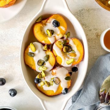 grilled peaches with coconut cream in a white dish with nuts and seeds surrounding it