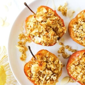 baked apples with a crumb topping on a white plate.