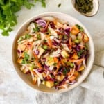 brown bowl of tropical mango coleslaw with mint next to it.