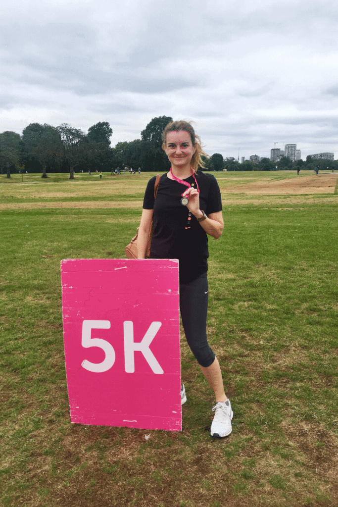 woman holding a medal after running a race next to a pink 5K sign.