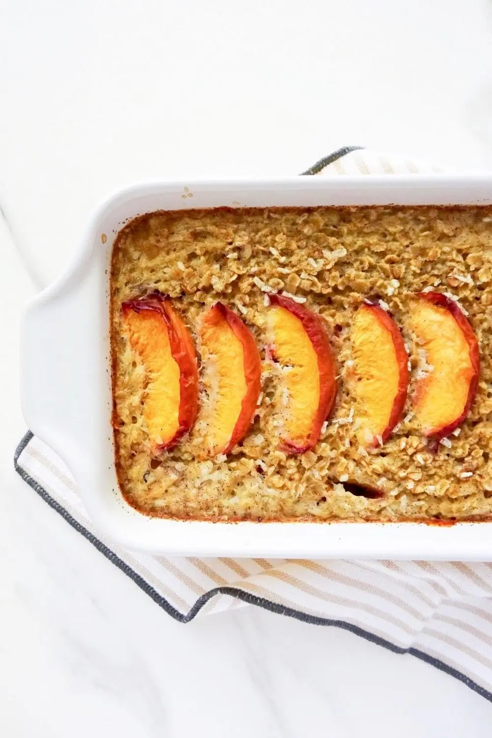 baked peach oatmeal in a white dish on a striped cloth.