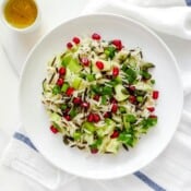 wild rice salad on a white plate with a small bowl of dressing next to it.