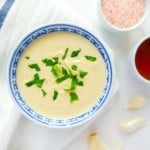 small blue and white bowl of tahini dressing next to small bowls of salt and maple syrup.