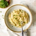 overhead view of a bowl of vegan cauliflower alfredo with a fork in it next to a bowl of herbs.