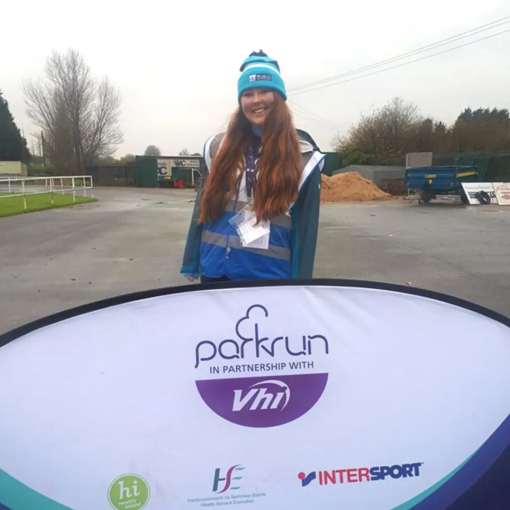 woman volunteering at Park Run behind a banner.