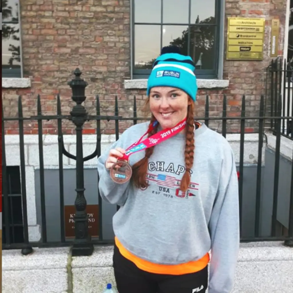 woman holding a running medal in front of railings.