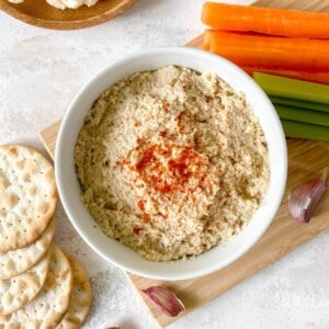cauliflower hummus in a white bowl surrounded by crudites and crackers.