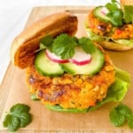 two sweet potato burgers with salad garnishes on a wooden board.