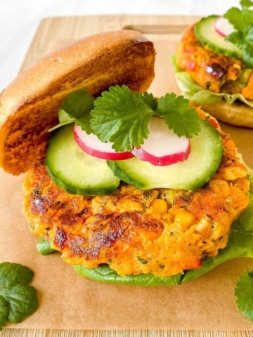 two sweet potato burgers with salad garnishes on a wooden board.