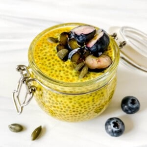 golden milk chia pudding in a glass jar with blueberries on top.