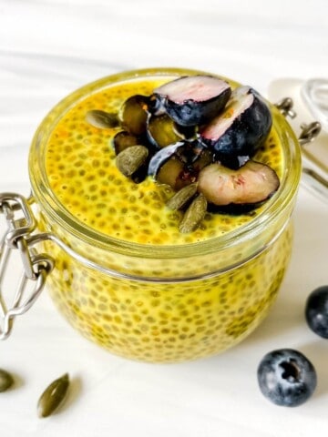 golden milk chia pudding in a glass jar with blueberries on top.