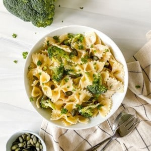 bowl of creamy tahini broccoli pasta next to broccoli and a bowl of pepitas.