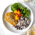 cod with mango salsa, rice and lettuce on a white plate next to a jar of sesame seeds.