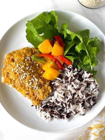 cod with mango salsa, rice and lettuce on a white plate next to a jar of sesame seeds.
