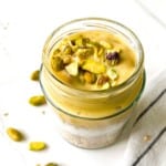 mango granola parfait in a glass jar with pistachios topping it next to a white and black striped cloth.