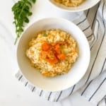 baked butternut squash in a white bowl on a white and black striped cloth next to salad leaves.