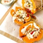 rice stuffed butternut squash on a wooden board next to a small bowl of tahini with a spoon in it.