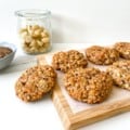 wooden board with coconut macadamia oat cookies on it with a glass jar of macadamias and bowl of flax in the background.