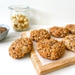 wooden board with coconut macadamia oat cookies on it with a glass jar of macadamias and bowl of flax in the background.