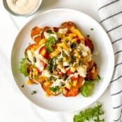 sweet potato nachos on a white plate on a striped cloth next to a small bowl of tahini.