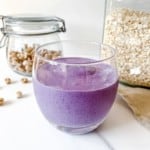 glass of tiger nut and blueberry smoothie with jars of oats and tiger nuts in the background.
