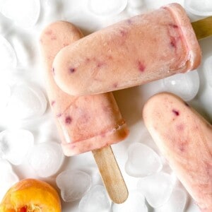 peaches and cream popsicles on ice cubes with fresh peaches next to them.