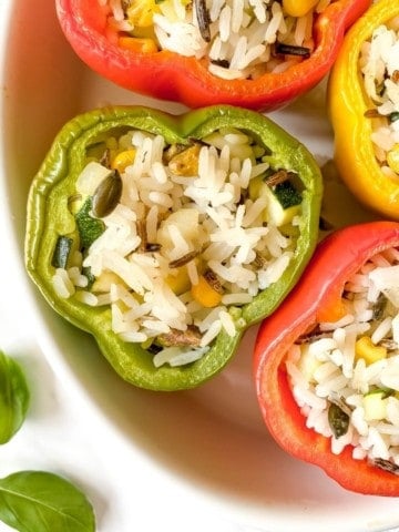 wild rice stuffed peppers in a white baking dish.