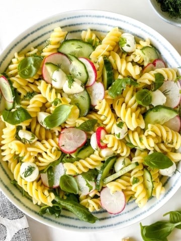 cucumber dill pasta salad in a white bowl with a blue striped rim.