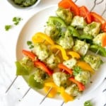 pesto chicken skewers on a white plate next to a bowl of pesto.