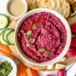 overhead view of a bowl of roasted beetroot hummus surrounded by crudites and crackers.