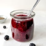 glass jar of blackberry chia jam with a spoon in it next to fresh blackberries.