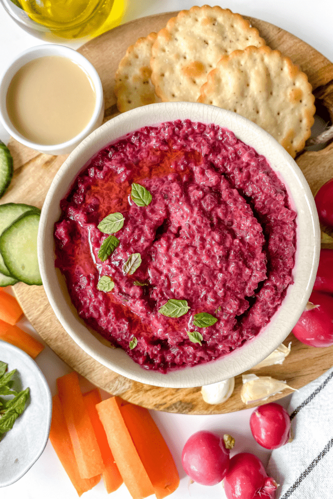 beetroot hummus surrounded by vegetables and crackers on a board
