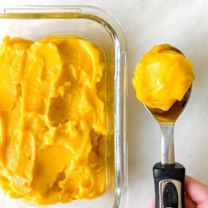 ice cream scoop of mango sorbet next to a glass dish of sorbet.