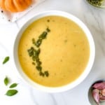 pumpkin pesto soup in a white bowl next to an orange pumpkin.