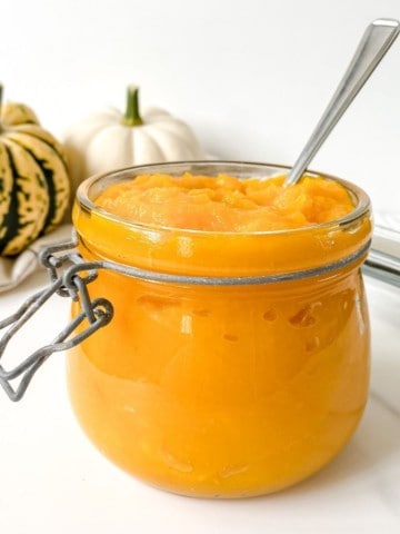 glass jar of pumpkin puree with a spoon in it.