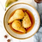 three spiced poached pears in a grey bowl with apple juice syrup.