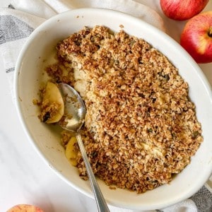cardamom apple crisp in a white dish with a spoon in it.