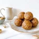 cardamom pistachio energy balls on a plate with a jug in the background.