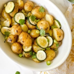 roasted potatoes with zucchini in a white dish.