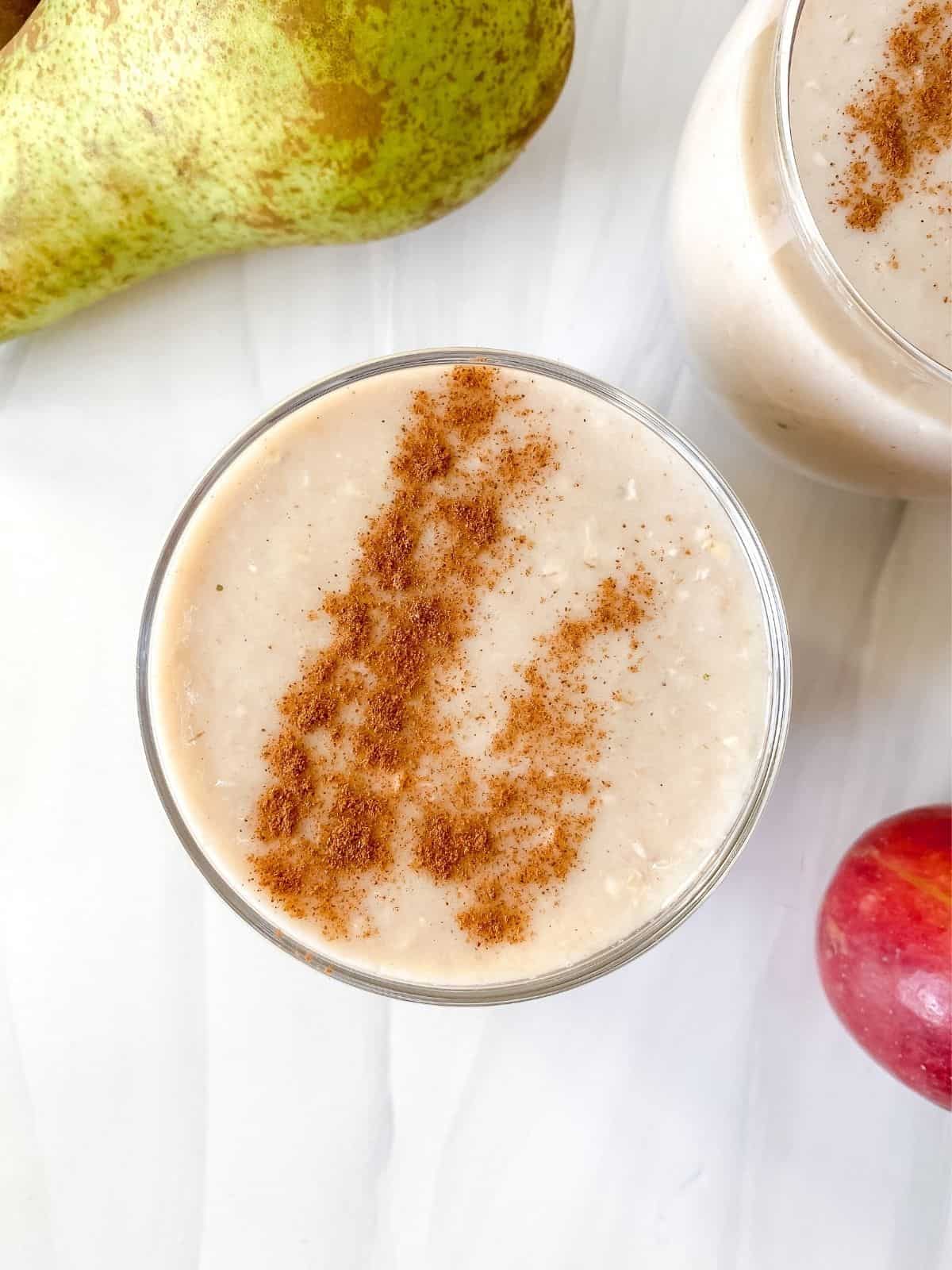 overhead view of apple and pear smoothie in a glass surrounded by pears and apples