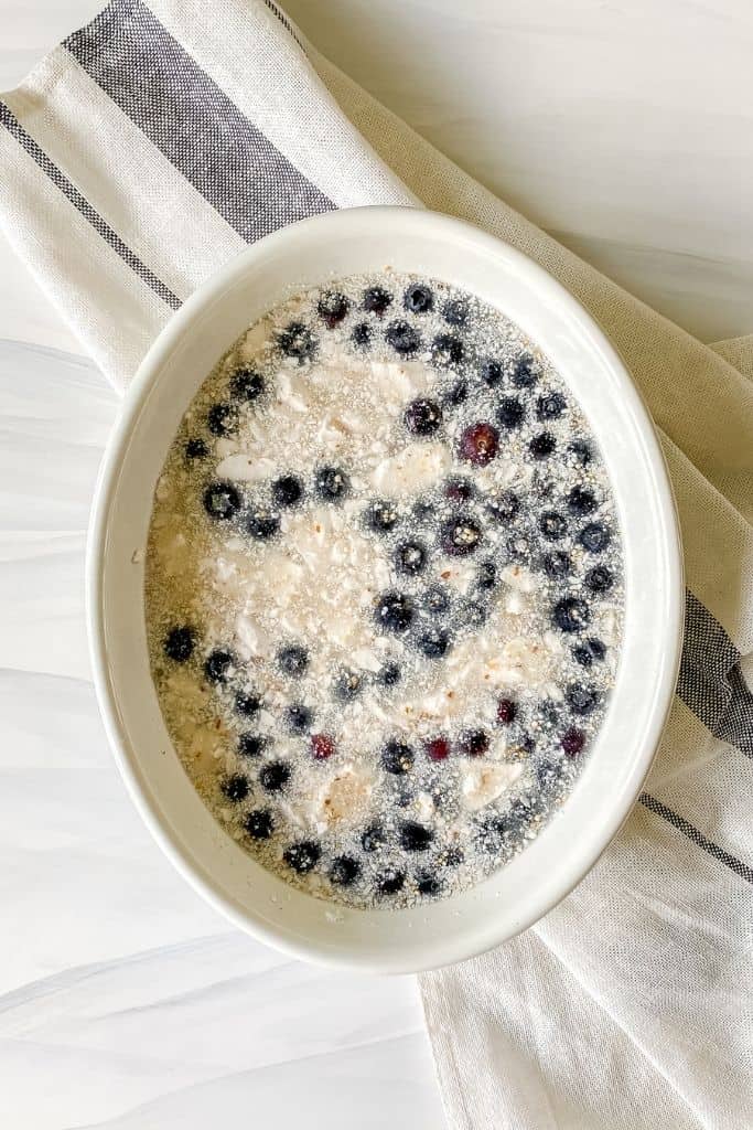 blueberries, quinoa and coconut milk mixed together in a white dish on a white and blue cloth.
