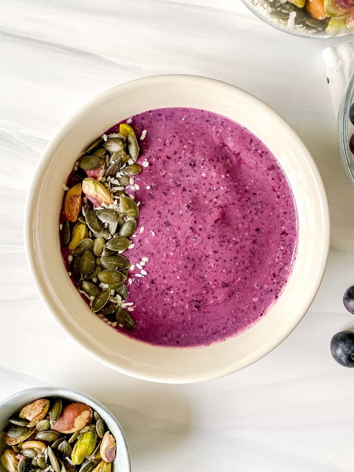 blueberry smoothie bowl with a bowl of seeds next to it.
