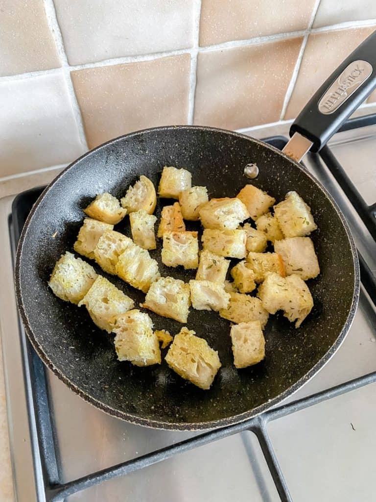 cubes of bread and oil in a pan on a stove top.