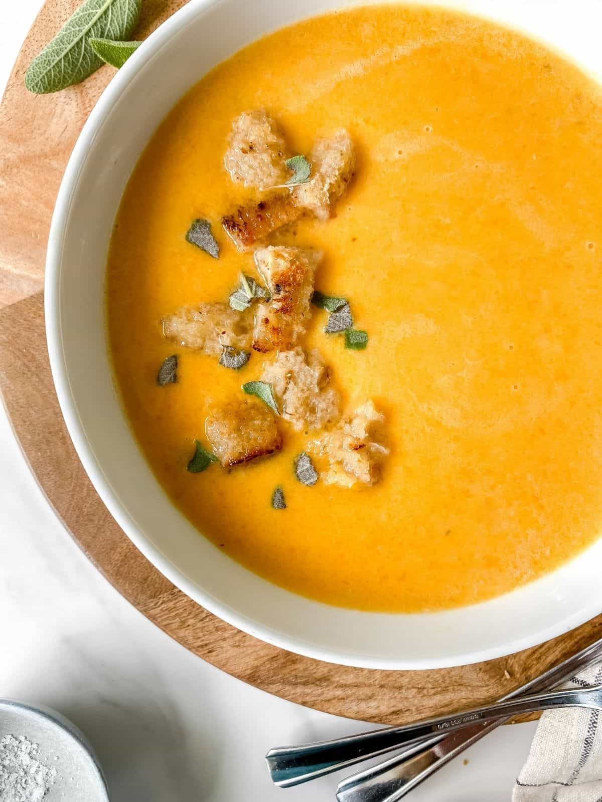 butternut squash and apple soup in a white bowl on a board.