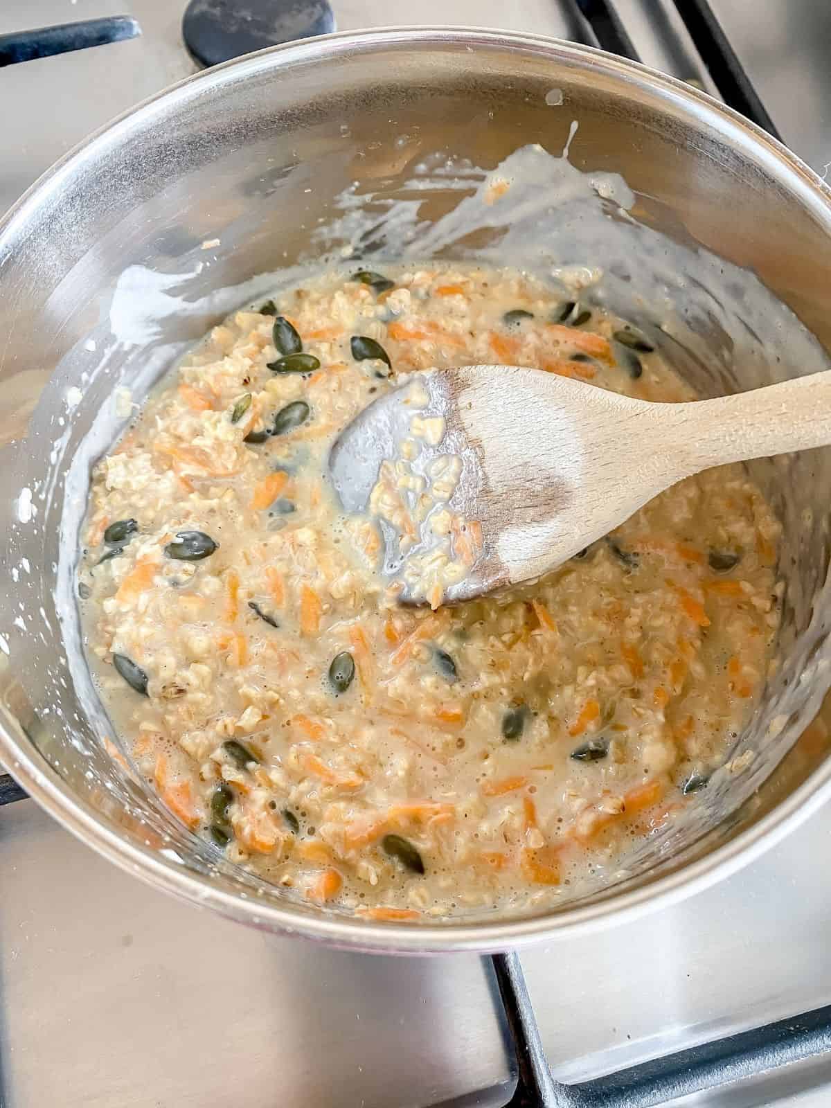 carrot cake porridge cooking in a pan with a wooden spoon in it on a stove top.