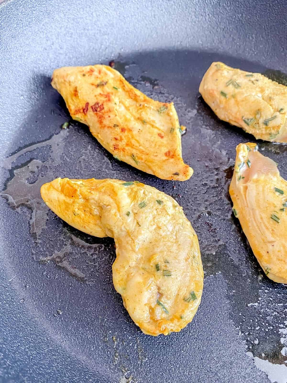 rosemary chicken pieces cooking in a black skillet.