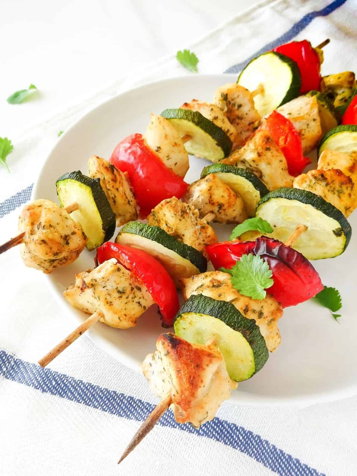 coconut chicken skewers on a white plate on a white and blue cloth.