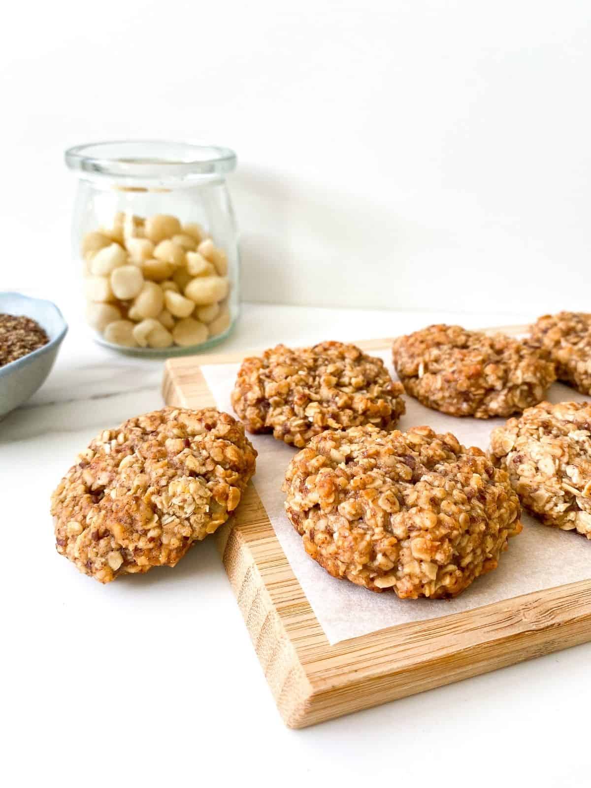 coconut macadamia nut cookies on a wooden board with a bowl of flax and jar of macadamias in the background.